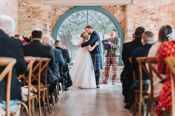 Bride and groom kiss at altar with celebrant smiling and clapping in background